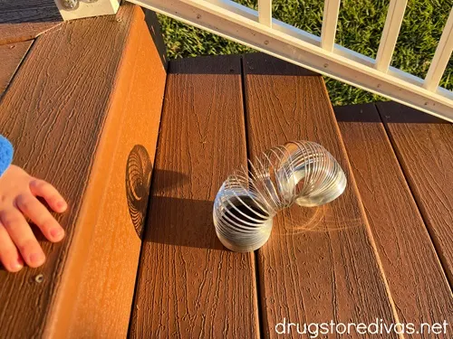 A young child's hand pushing a Slinky toy down the stairs.