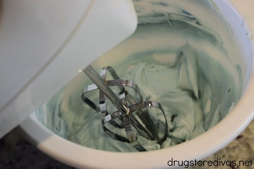 A hand mixer mixing blue frosting in a white bowl.