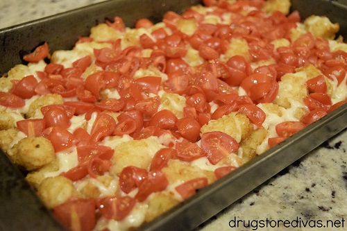 Cherry tomatoes and mozzarella cheese on top of tater tots in a cake pan.