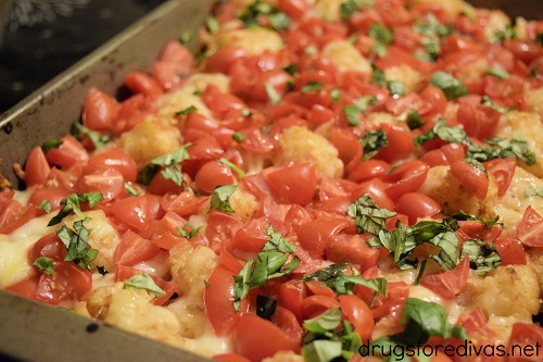 Basil, cherry tomatoes, and mozzarella cheese on top of tater tots in a cake pan.