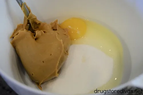 Peanut butter, sugar, and an egg in a white bowl.