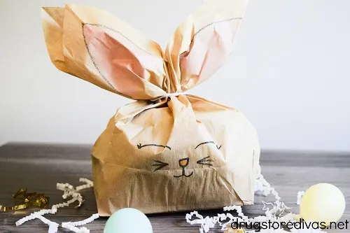A Paper Bag Bunny behind paper shred and plastic Easter eggs.
