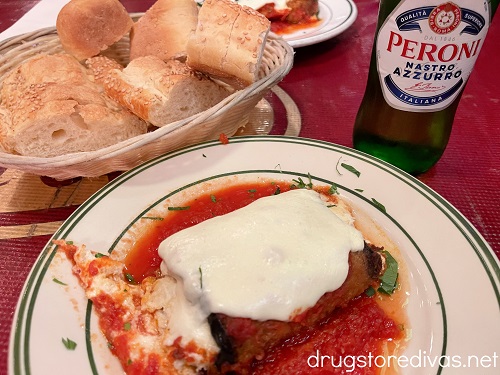 Eggplant rollatini, a basket of bread, and a Peroni beer on a table.