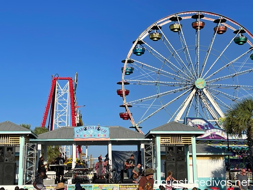A band on stage at the Carolina Beach Pavilion with a giant slide and ferris wheel in the background.