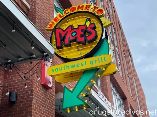 A neon sign with an arrow pointing towards a brick building advertising Moe's Southwest Grill.