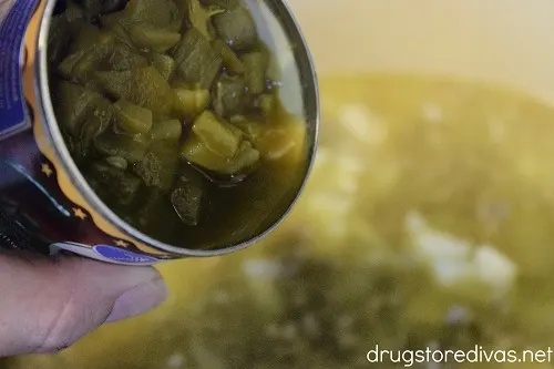 A can of green chilis being poured into soup in a Dutch oven.