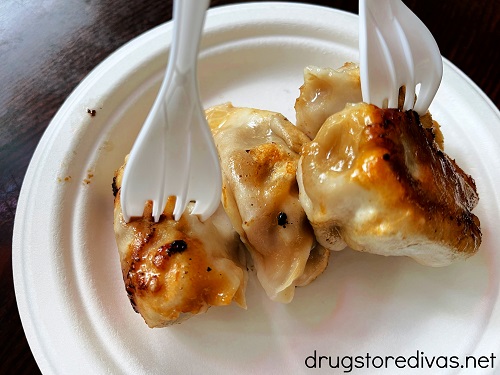Four dumplings on a white paper plate with two forks in the dumplings.
