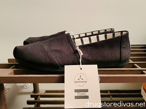 A pair of black Toms slip on sneakers, with the tag on, on a shoe rack.