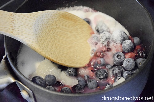 Sugar and blueberries in a pan being stirred with a wooden spoon.