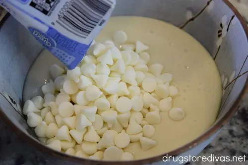 White chocolate chips being poured into a bowl that has sweetened condensed milk in it.