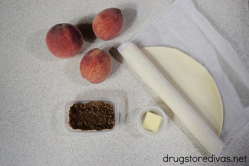 Three peaches, brown sugar, butter, and pie crust on a counter.