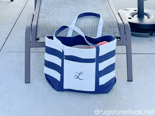 A blue and white striped pool bag with the letter L on it in front of a lounge chair.