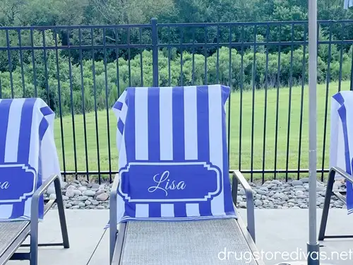 A blue and white striped towel that says "Lisa" on it on the back of a lounge chair at the pool.
