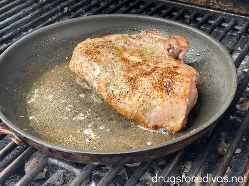 A pork chop in a cast iron skillet on a grill.