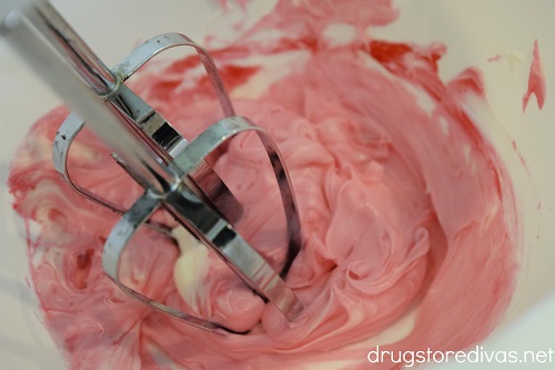 Pink frosting in a bowl with a hand mixer.