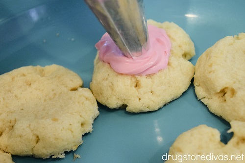 Pink icing being piped into thumbprint cookies.