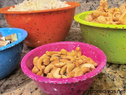 Four Zak brand confetti bowls: a large orange one with popcorn, a neon green one with pork rinds, a pink one with mixed nuts, and a blue bowl to the side.