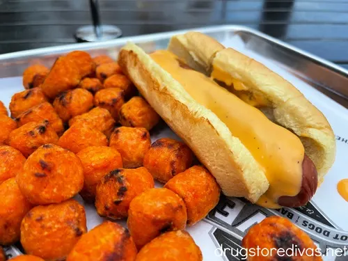 A hot dog with cheese next to sweet potato tater tots from Crave Hot Dogs.
