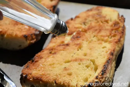Salt being sprinkled on a toasted loaf of bread.