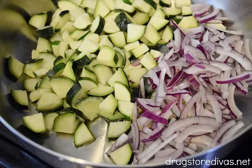 Quartered zucchini and sliced red onion in a silver pan.
