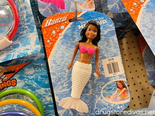 A mermaid toy in its package hanging from a peg in a store.