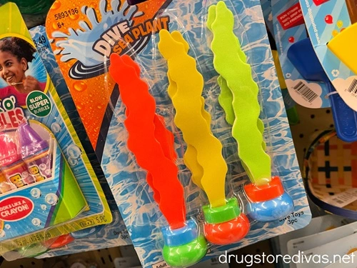 A three pack of seaweed shaped pool dive toys, that are orange, yellow, and neon green, in a pack on a shelf in a store.