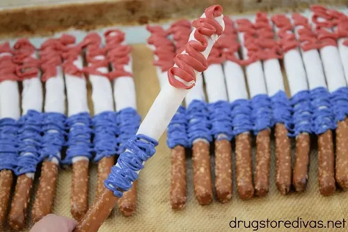 A hand holding a red, white, and blue chocolate pretzel above a bunch of other red, white, and blue chocolate covered pretzels.