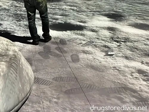 A man walking on a projection of the surface of the moon and footsteps are behind him.