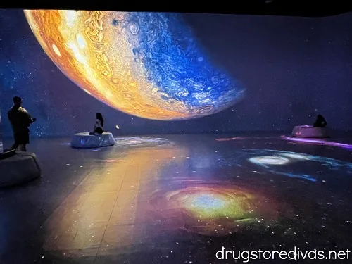 A planet on a wall and projections on the floor, inside of the Illuminarium Las Vegas.