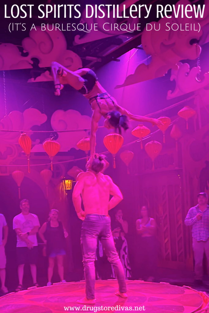 A female contortionist balancing on a man's head on a stage with the words "Lost Spirits Distillery Review (It's a Burlesque Cirque du Soleil)" digitally written above them.