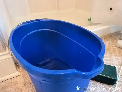 A blue bucket on the floor in front of a shower.