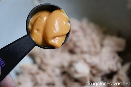A tablespoon of an orange mayo over tuna fish in a bowl.