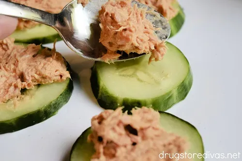 Tuna fish on a spoon being put on top of cucumber slices.