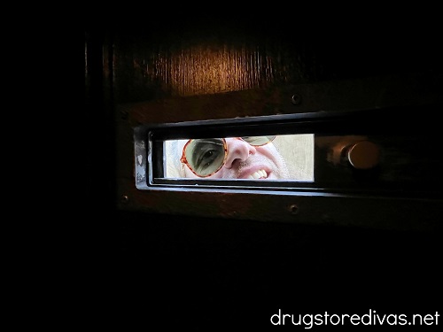 A man looking through a sliding peephole in a door.
