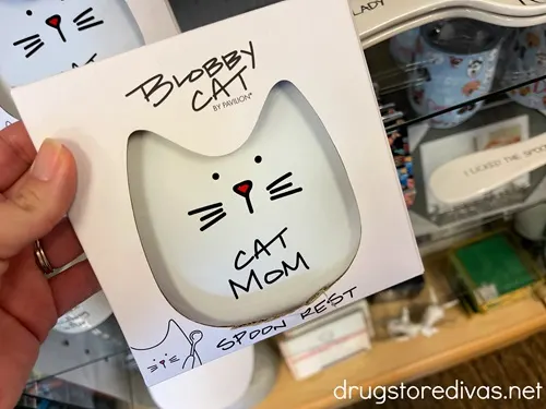 A hand holding a spoon rest shaped like a cat face that says Cat Mom on it.