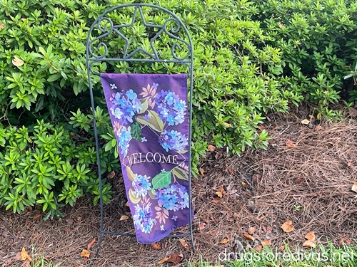 A purple outdoor garden flag with flowers on it on a metal hanger.