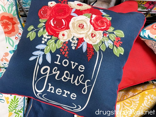 A blue pillow with a flower pot and flowers on it that says "love grows here" on it.