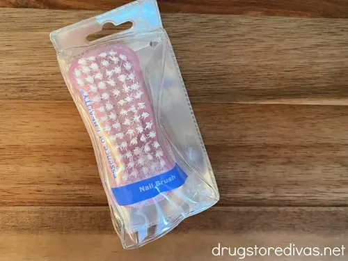 A pink nail brush in a package on a piece of wood.