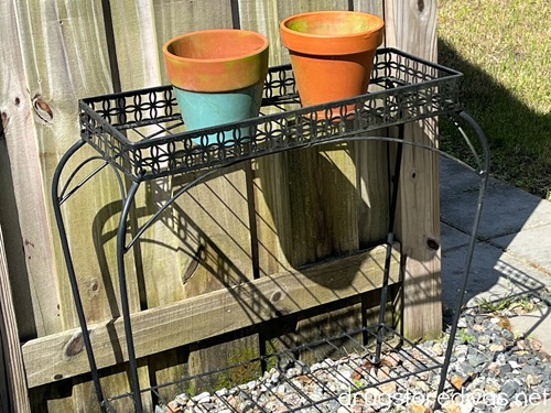 Two terra cotta pots on an outdoor metal plant stand against a wooden fence. 