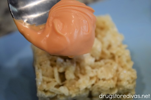 A spoon of melted orange candy melts over a Rice Krispies Treat.