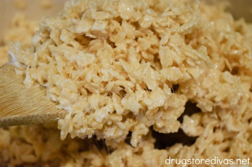 A Rice Krispies Treats mixture being stirred with a wooden spoon.