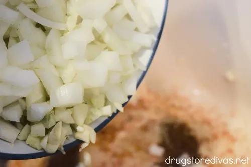 Chopped onion and garlic being poured into a Dutch oven.