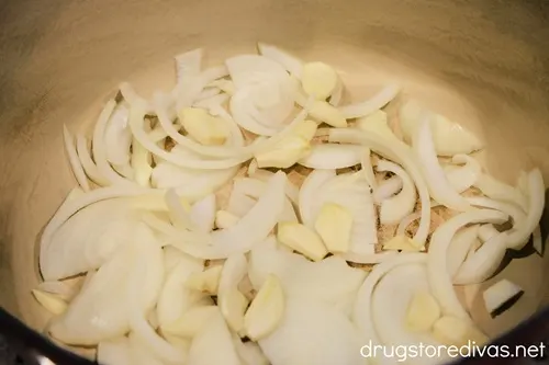 Sliced onions and garlic in the bottom of a Dutch oven.