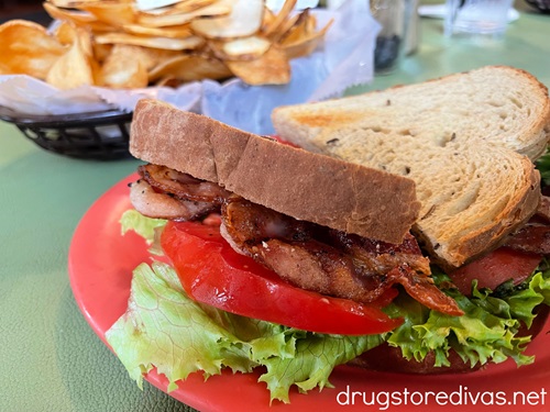 A BLT on a plate with homemade chips on a plate behind it.
