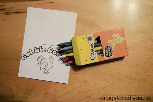 A coloring page with a turkey and gobble gobble on it and a pack of open crayons next to it.