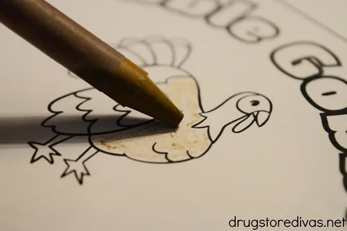 A brown crayon coloring a turkey coloring page.
