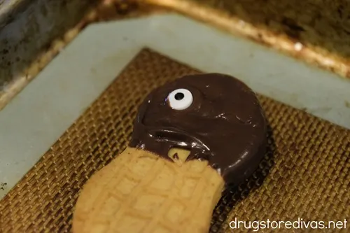 A candy eyeball stuck into melted chocolate on a Nutter Butter cookie.