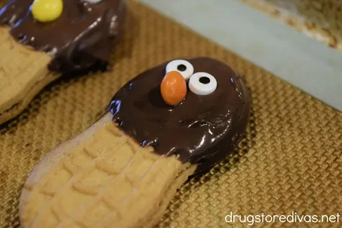 Two candy eyeballs and an orange mini Reese's pieces candy stuck into melted chocolate on a Nutter Butter cookie.
