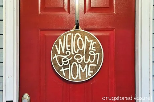 A round wooden sign that says "welcome to our home" on it made by Vinylbypanch.