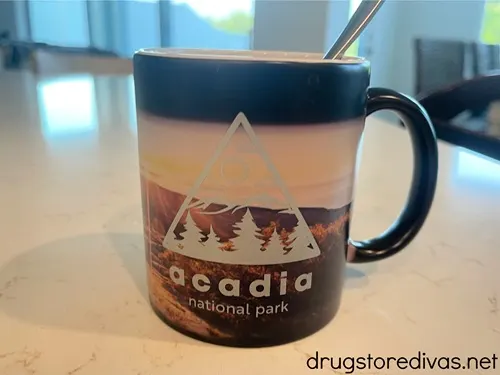 A black Arcadia National Park mug with a spoon in it on a counter.